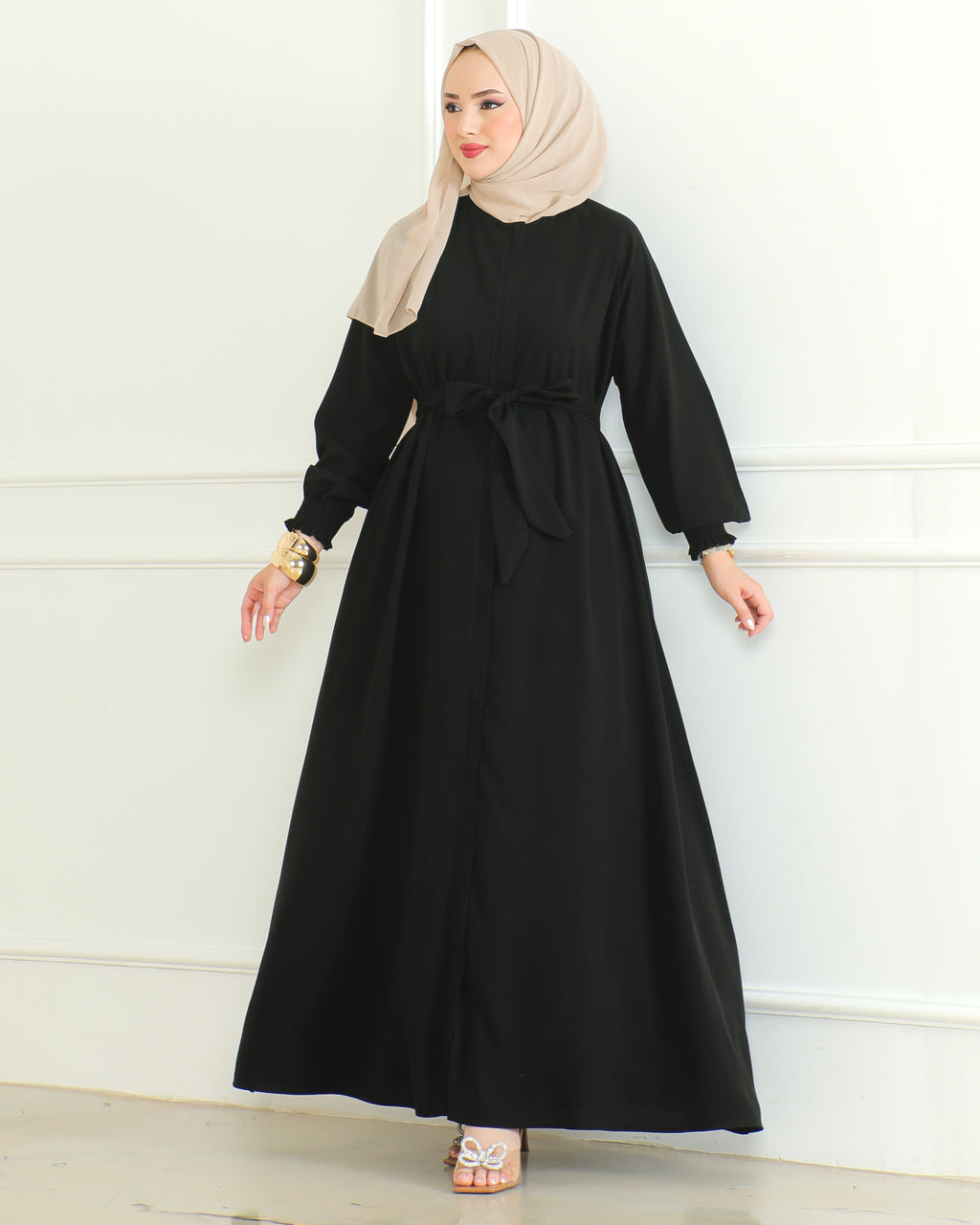 Black belted Turkish abaya with front zipper and elasticated ruffled cuffs, worn with a beige hijab – front view