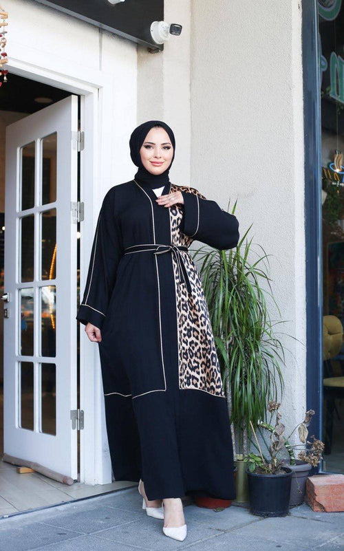 Woman wearing black Turkish abaya with leopard-print front panel and contrast trim, belted at waist, full-length front view
