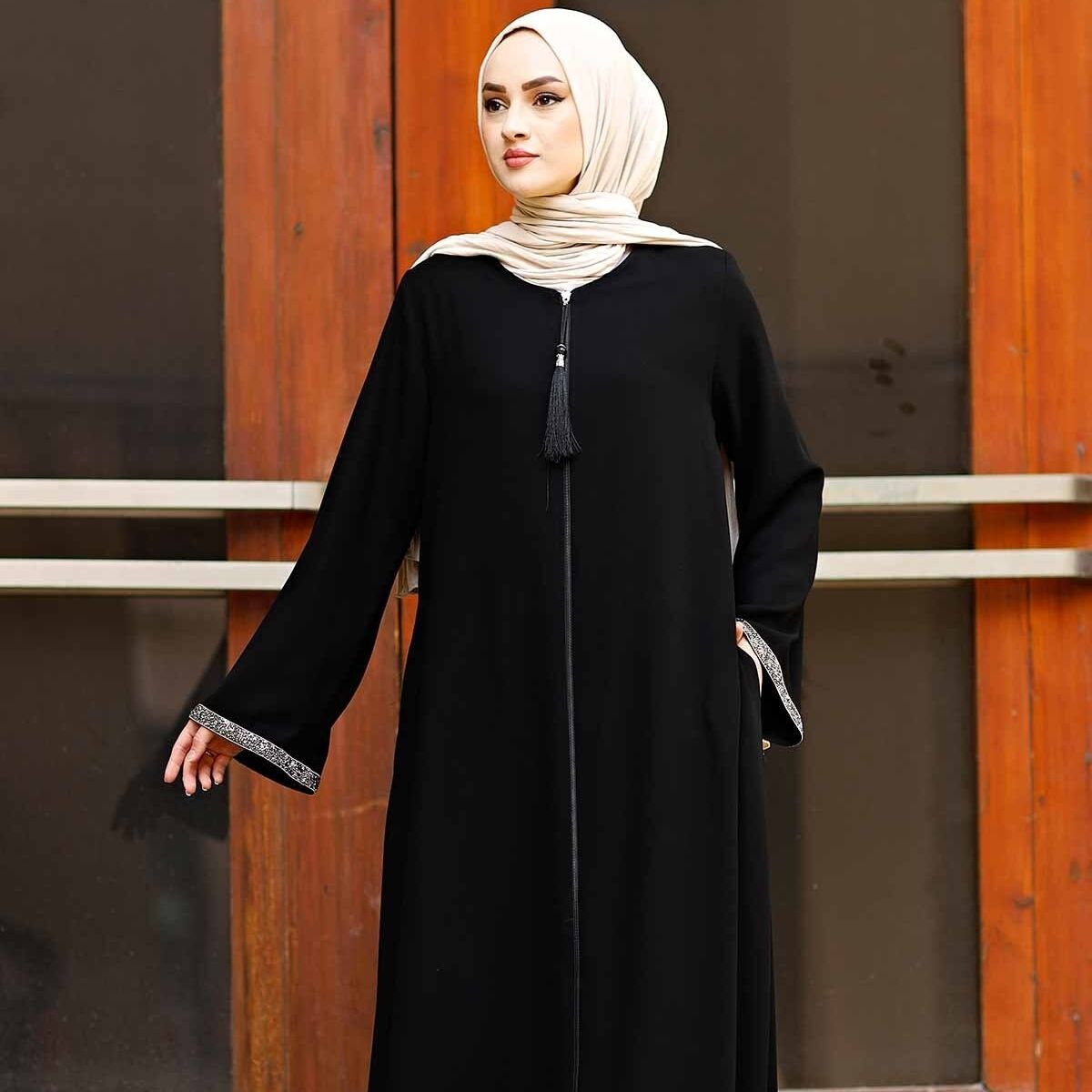 Woman wearing a black Turkish abaya with stone-trimmed flared cuffs and front tassel zipper, full-length front view